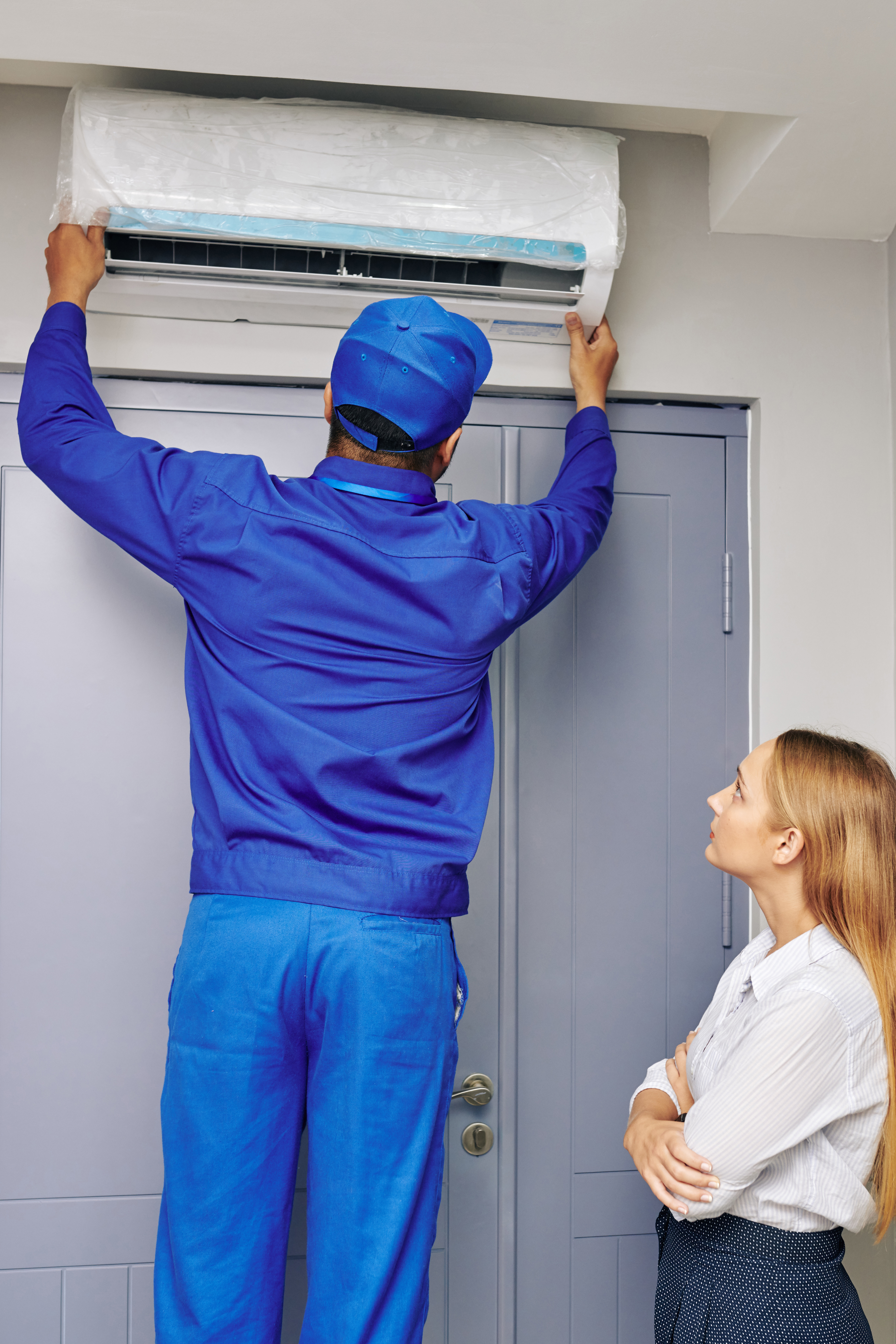 Young businesswoman looking at technician instaling air conditioner in office