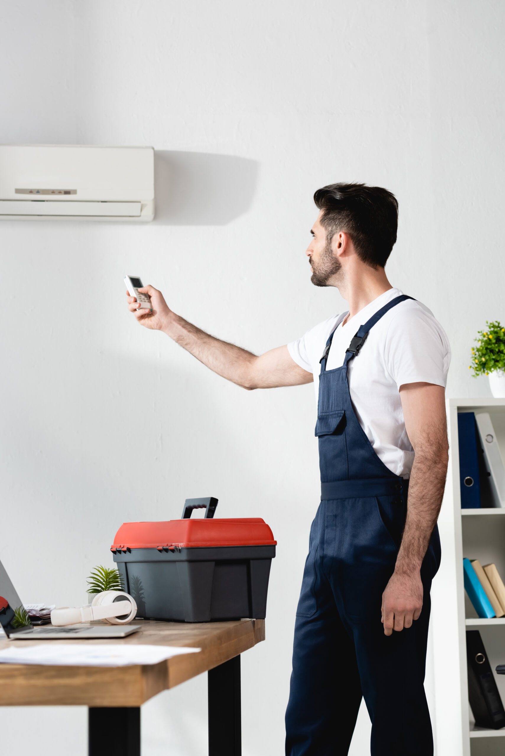 repairman using air conditioner remote controller while standing near toolbox